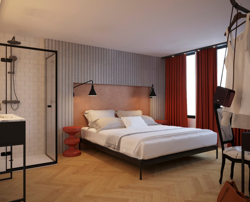 Chambre d'hôtel moderne Ibis_KAI avec un grand lit aux draps blancs, flanqué de tables de chevet rouges et d'appliques murales noires. À gauche, il y a une douche vitrée avec des carreaux de métro blancs. Des rideaux rouges couvrent les fenêtres et quelques vêtements et accessoires sont suspendus sur un portant dans le coin.