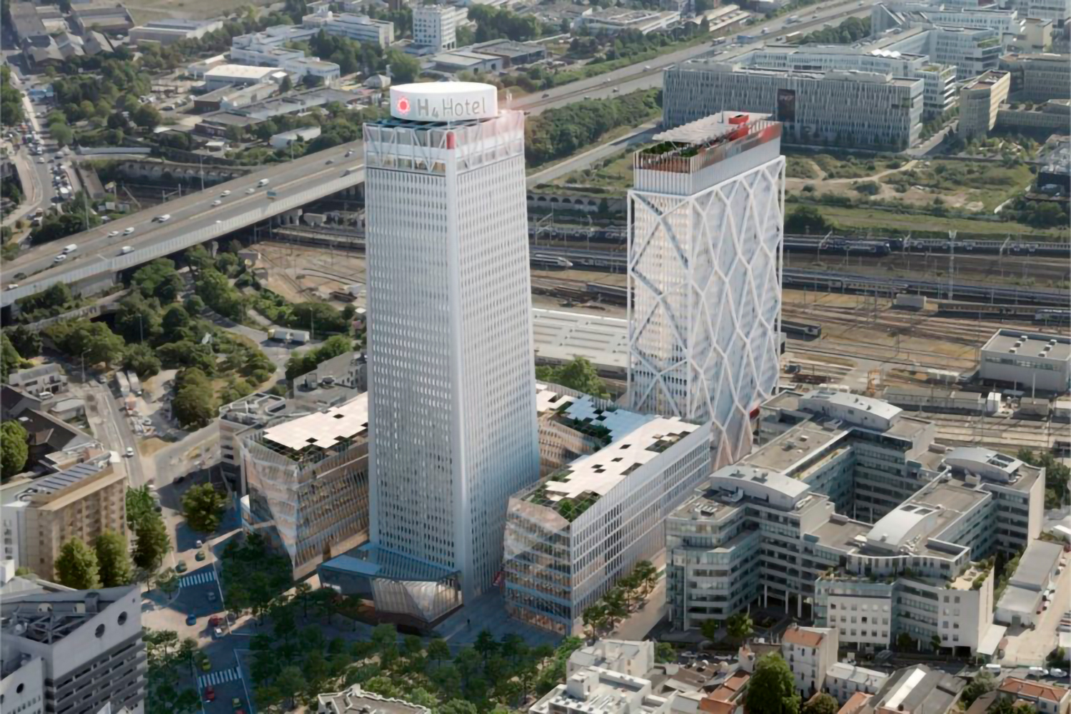 Vue aérienne d'une zone urbaine moderne avec deux immeubles de grande hauteur et le logo de l'hôtel H4 au sommet de l'une d'elles. À proximité, un hôtel Ibis se dresse en évidence parmi les routes environnantes, la verdure, les voies ferrées et divers autres bâtiments. Le ciel clair renforce l'atmosphère dynamique et animée.